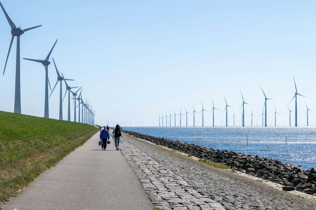 Küstenweg mit zwei Spaziergängern und zahlreichen Windrädern am Meer
